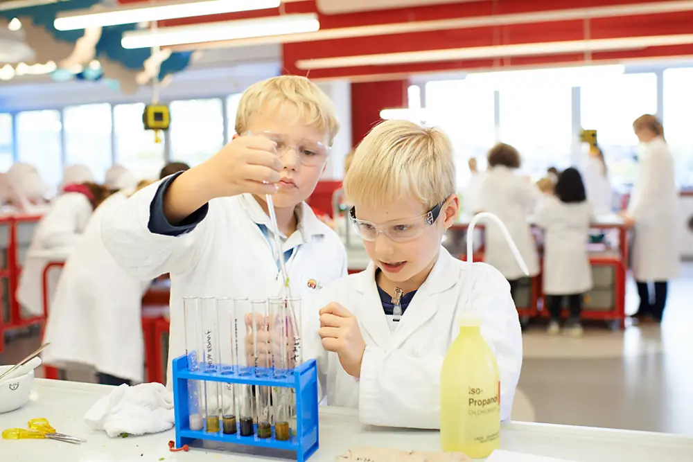 Zwei Jungen in Laborkitteln mit Pipette tropfen eine Lösung in Reagenzgläser. 