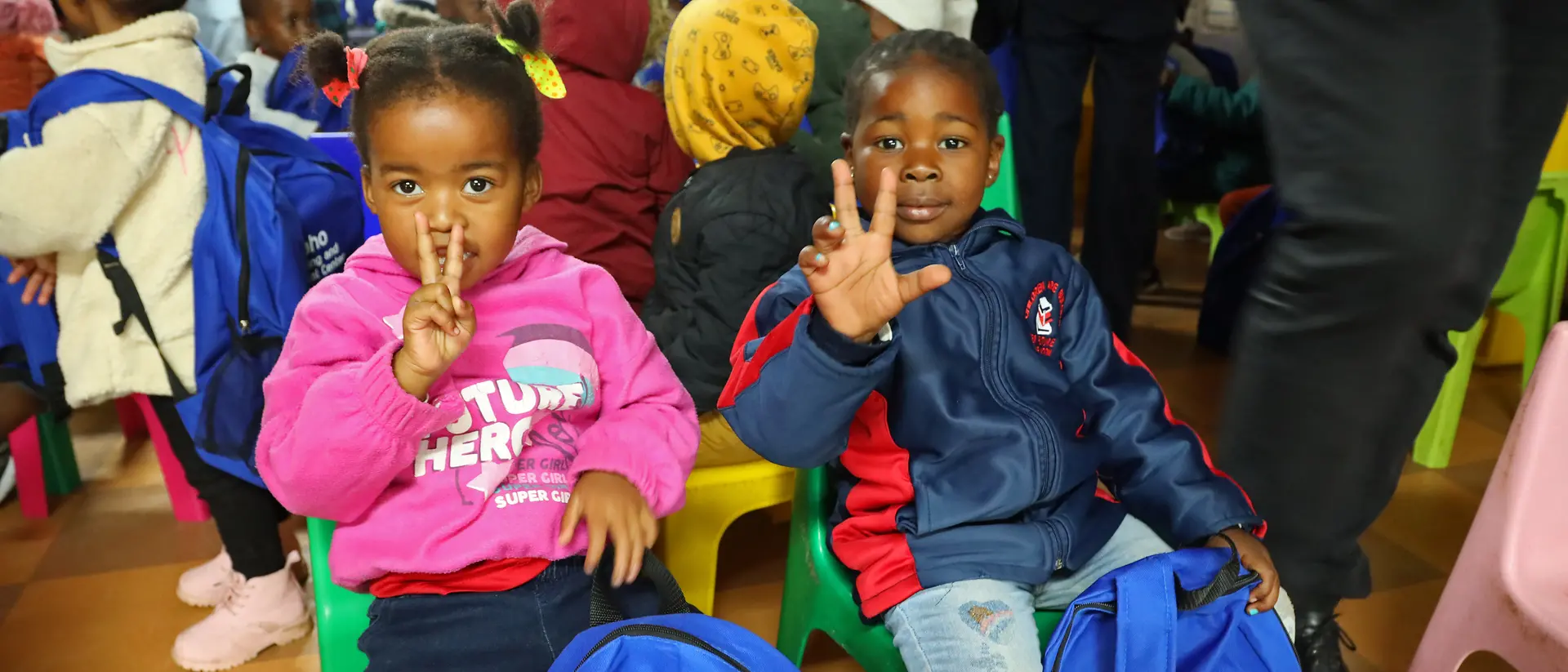 Zwei kleine Kinder sitzen nebeneinander und halten ihr Finger hoch.