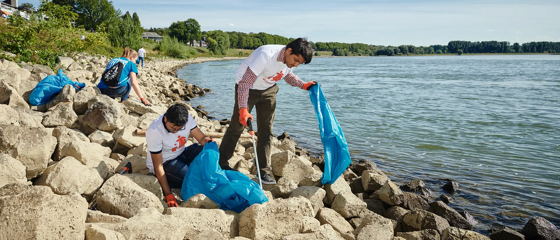 Eine kleine Gruppe von Menschen sammelt Müll an einem Ufer.