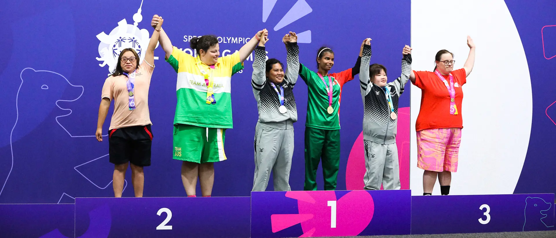 Sechs Athletinnen stehen auf dem Siegerpodest bei den Special Olympics und strecken die Arme in die Luft.