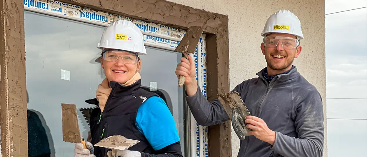 Drei Henkel-Freiwillige führen Renovierungsarbeiten am Fensterrahmen eines Hauses durch.