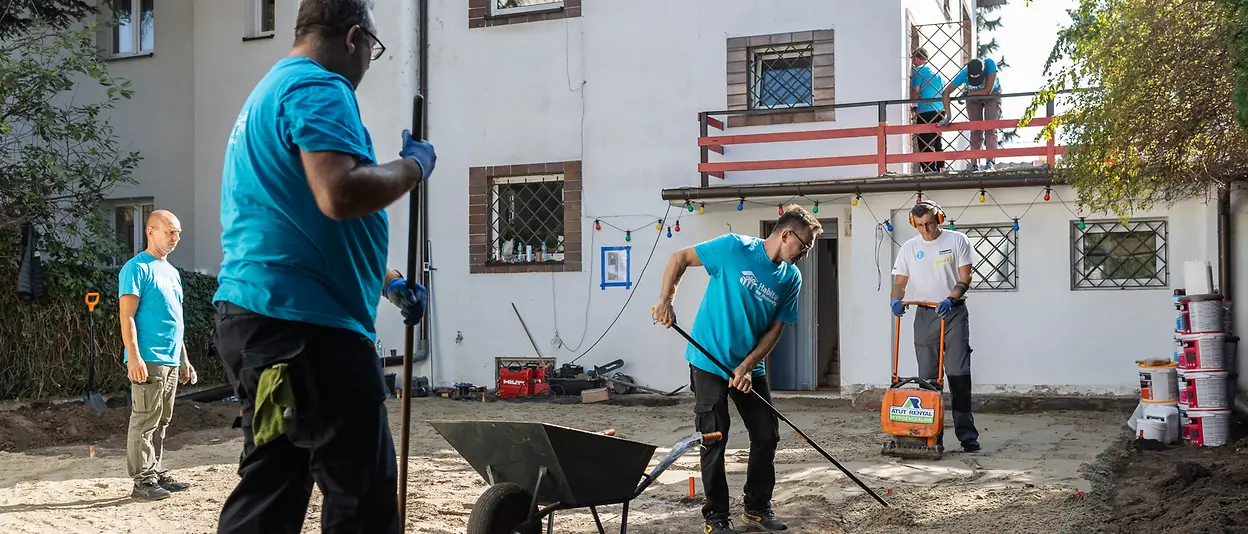 Die Freiwilligen bereiten den Garten des Hauses für die Verlegung der Terrassensteine vor.