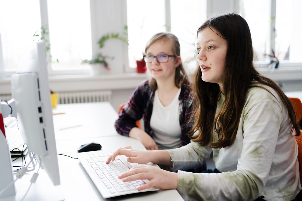 Eine Hochschulabsolventin unterstützt eine Schülerin an einem Computer.