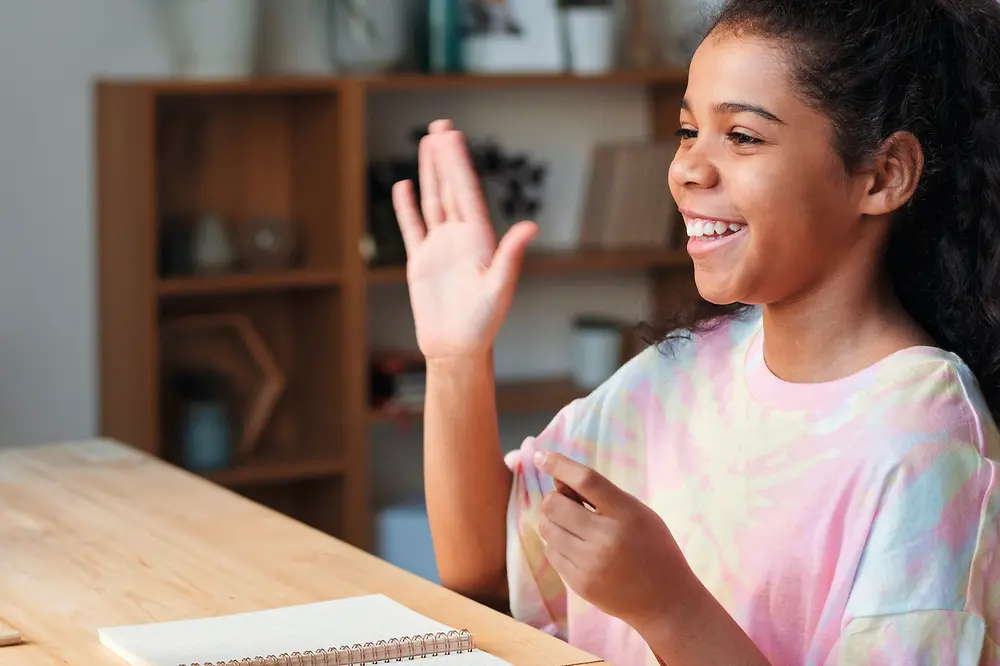 Ein Kind schaut auf den Bildschirm eines Laptops und hebt die Hand. 