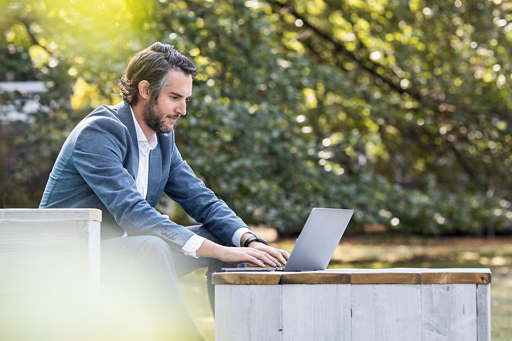 Flexibles und ortsunabhängiges Arbeiten: Ein Mann arbeitet draußen an seinem Laptop, umgeben von der Natur.