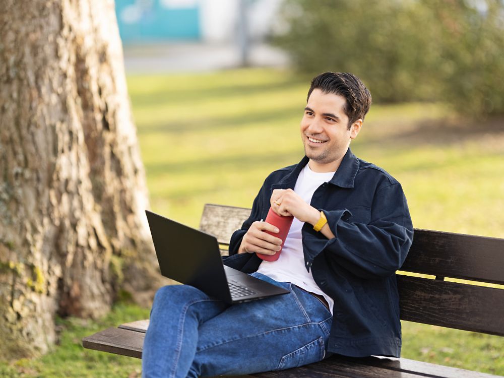 Ein Henkel-Mitarbeiter sitzt auf einer Parkbank und arbeitet an seinem Laptop. 