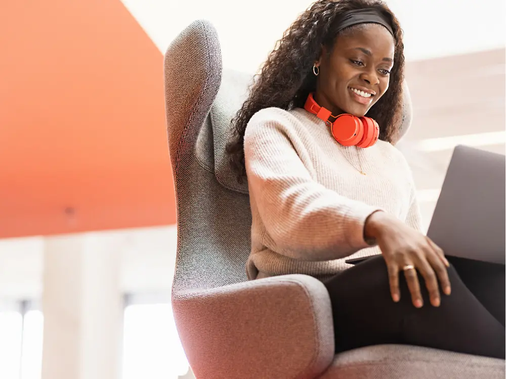 Eine Henkel-Mitarbeiterin sitzt mit ihrem Laptop auf den Knien in einem bequemen Sessel. Sie lächelt. 