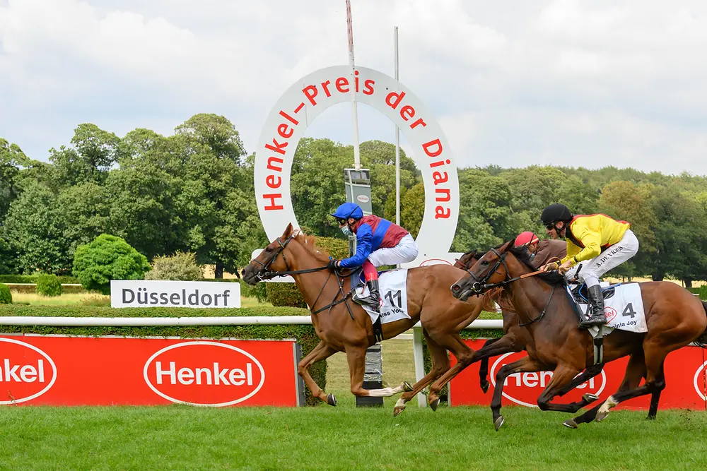Drei Jockeys liefern sich beim Henkel-Preis der Diana auf ihren Pferden ein Kopf-an-Kopf-Rennen