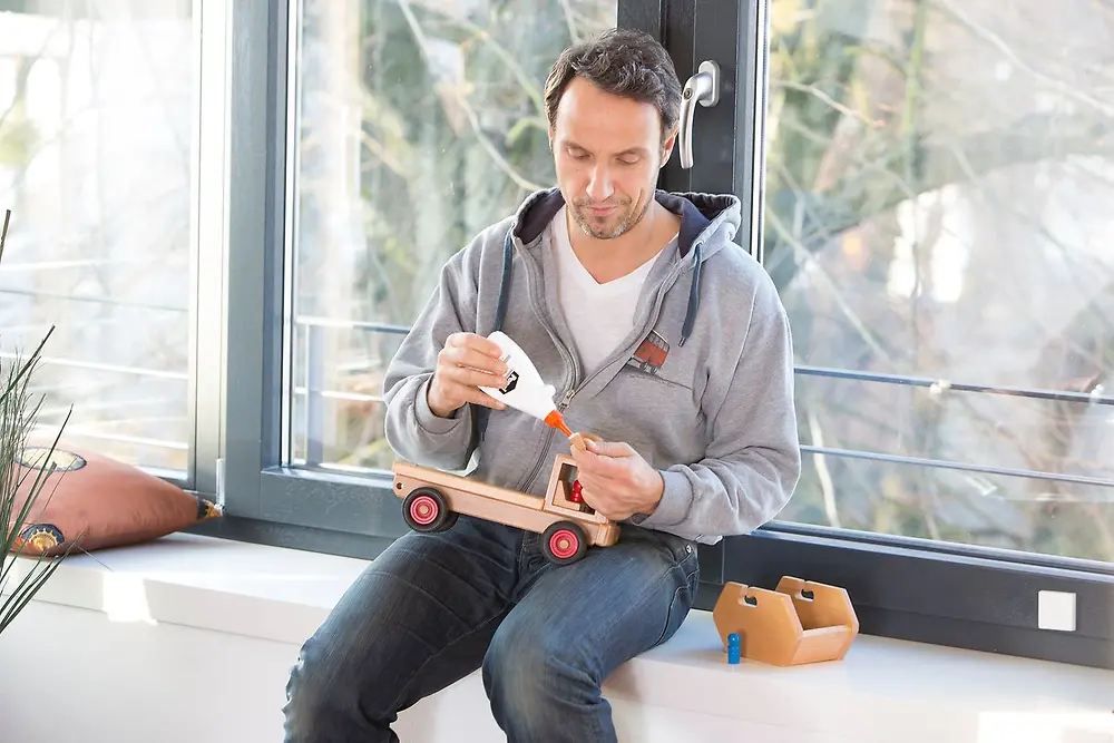Ein Mann repariert ein hölzernes Spielzeugauto mit Ponal Holzleim