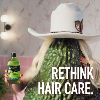 Eine Nature Box Shampoo-Werbung mit der Cowboyhut-tragenden blonden Avocado.