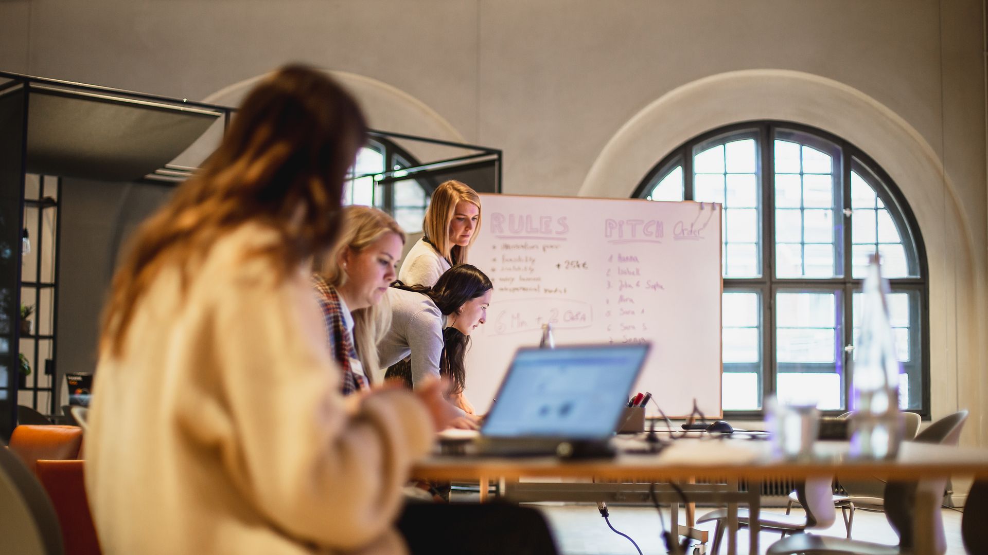 Frauen arbeiten an Laptops vor einem Flipchart.