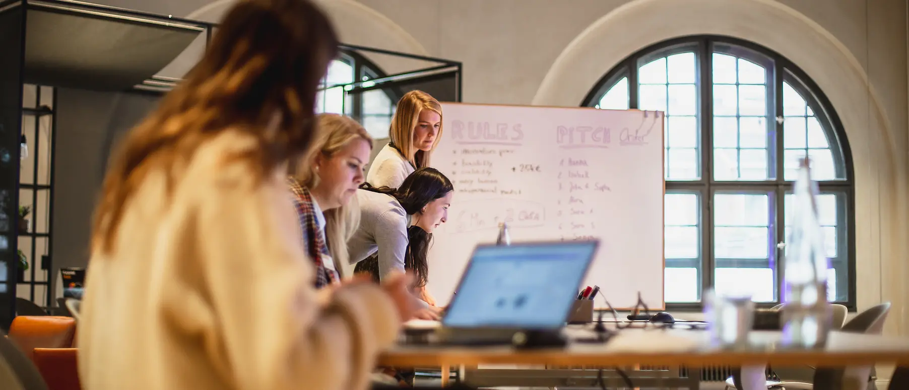 Frauen arbeiten an Laptops vor einem Flipchart.