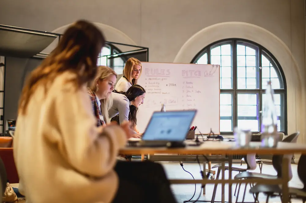 Frauen arbeiten an Laptops vor einem Flipchart.