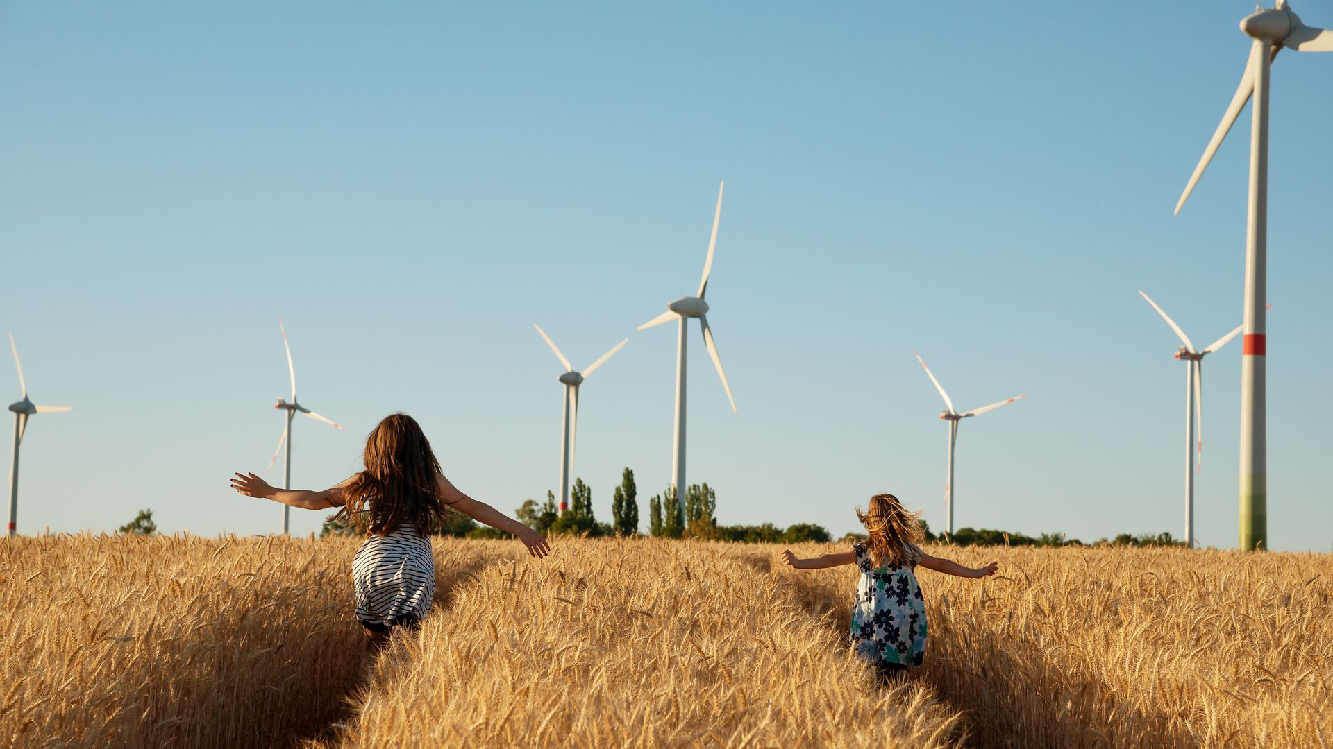 Mädchen laufen durch ein Feld auf Windräder zu.