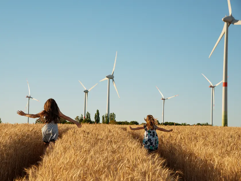 Mädchen laufen durch ein Feld auf Windräder zu.
