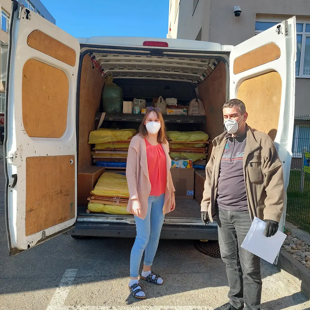 Eine Frau und ein Mann stehen vor einem Transporter, der mit Kinderbetten beladen ist, die gespendet werden.