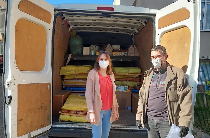 Eine Frau und ein Mann stehen vor einem Transporter, der mit Kinderbetten beladen ist, die gespendet werden.