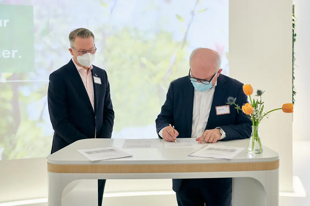 Zwei Vertreter von BASF und Henkel stehen an einem Tisch und unterschreiben den Vertrag.