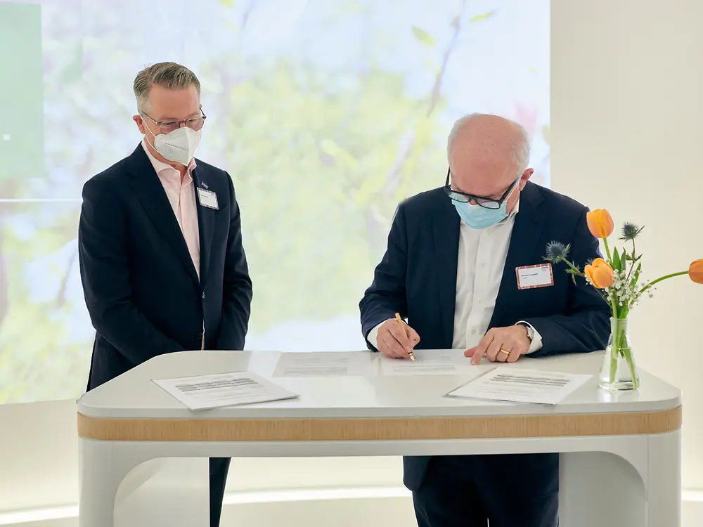 Zwei Vertreter von BASF und Henkel stehen an einem Tisch und unterschreiben den Vertrag.