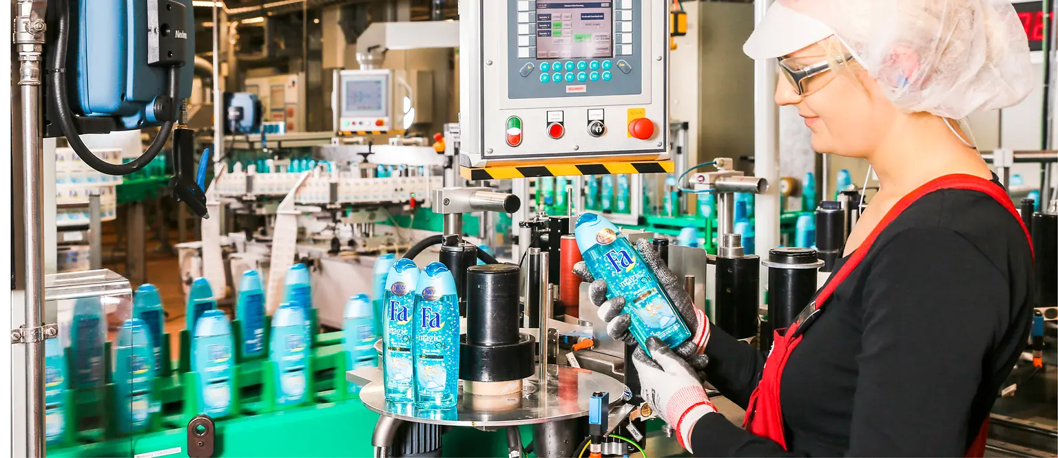 Eine Mitarbeiterin steht am Fließband und überprüft eine Fa-Flasche.