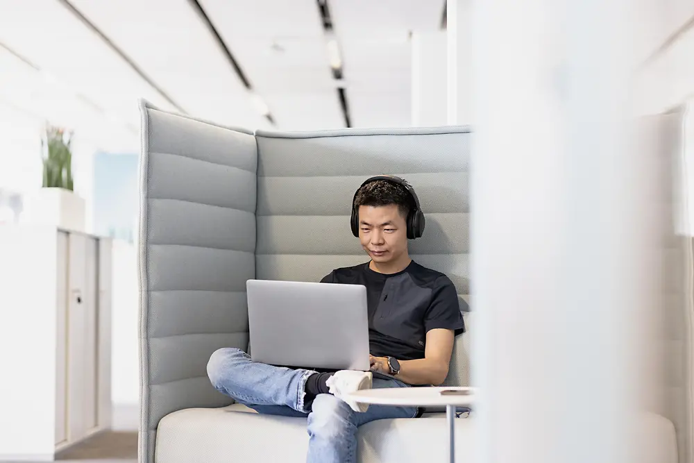 Ein Mann sitzt mit Kopfhörern auf einem Sessel und arbeitet an einem Laptop