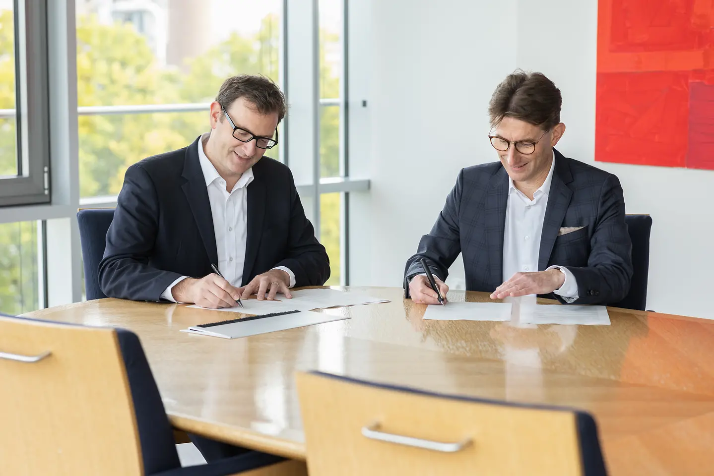 Zwei Männer unterzeichnen einen Vertrag in einem Konferenzraum.