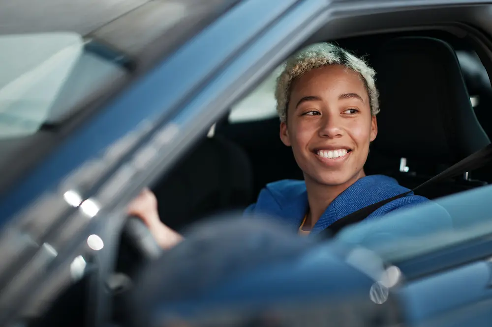 Eine Fahrerin sitzt in ihrem E-Auto und lächelt