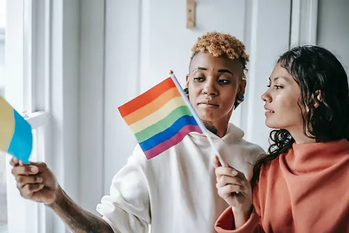 Zwei Frauen unterhalten sich miteinander und halten eine LGBTQ+-Flagge in der Hand. 