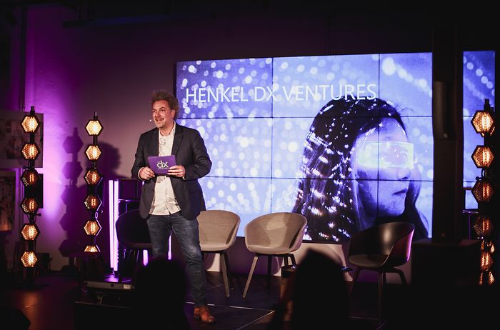 Marc Thom steht auf der Bühne vor einem LED-Bildschirm auf dem “Henkel dx Ventures” steht.