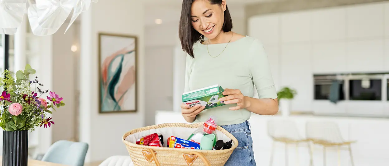 Eine Frau steht an einem Esstisch und hält die Persil Power Bars in der Hand. 