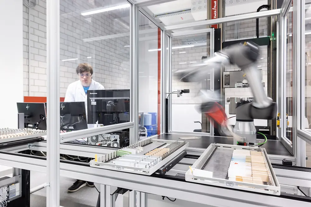 In einem automatisierten Labor arbeitet ein Roboterarm an Klebstofftechnologien.