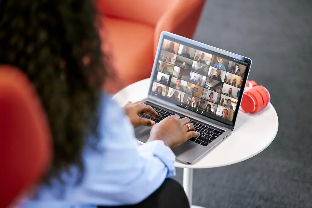 Eine Mitarbeiterin sitzt an einem Tisch und nimmt über ihren Laptop an einem digitalen Zusammenkommen mit ihren Kolleg:innen teil. 