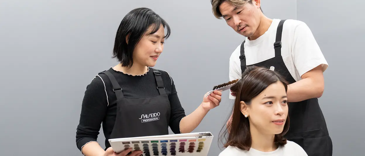 Zwei Haarpflegeexpert:innen führen eine Haarfarbenanalyse bei einer Konsumentin durch.