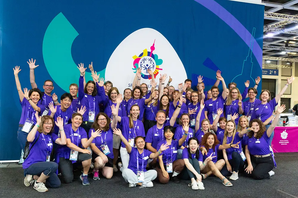 Das internationale Team von 60 Henkel-Freiwilligen steht jubelnd vor dem Banner der Special Olympics World Games in Berlin.