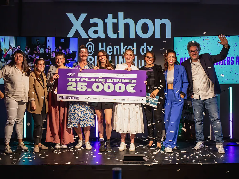 Die Xathon-Gewinner:innen des letzten Jahres stehen gemeinsam mit Vertreter:innen von Henkel dx Ventures auf der Bühne und freuen sich über einen symbolischen Scheck von 25.000 Euro.