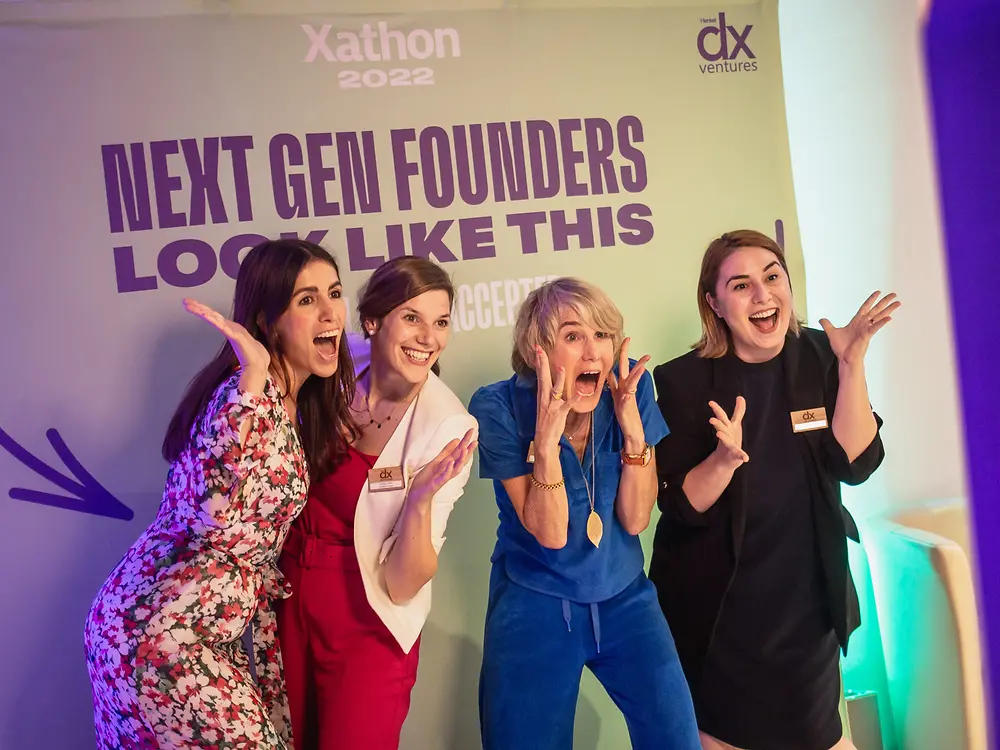 Vier Unternehmerinnen stehen vor einer Fotowand mit der Aufschrift "Next gen founders look like this". 