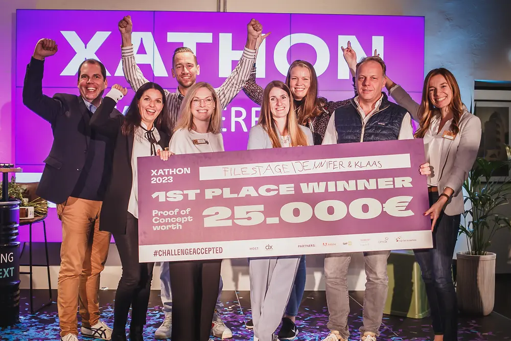 Drei Männer und fünf Frauen stehen jubelnd auf der Bühne und halten einen Scheck mit der Aufschrift „1. Platz Gewinner Proof of Concept im Wert von 25.000 Euro."