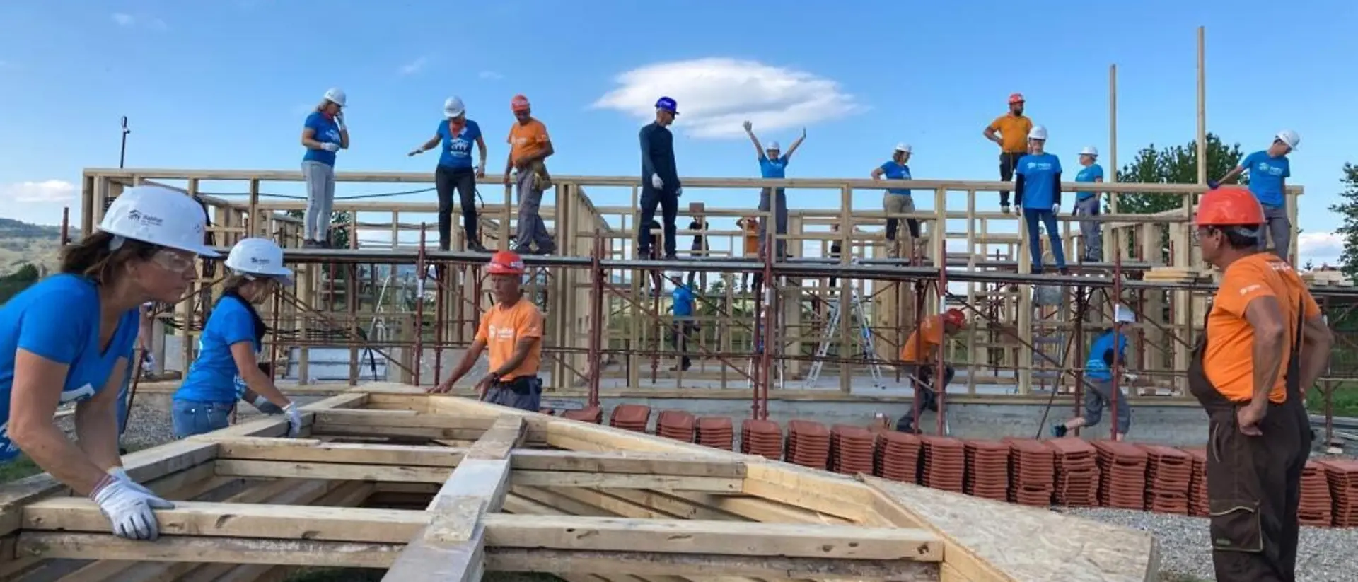 Eine große Gruppe von ehrenamtlichen Helfern hilft auf einer Baustelle mit, ein Haus zu bauen.