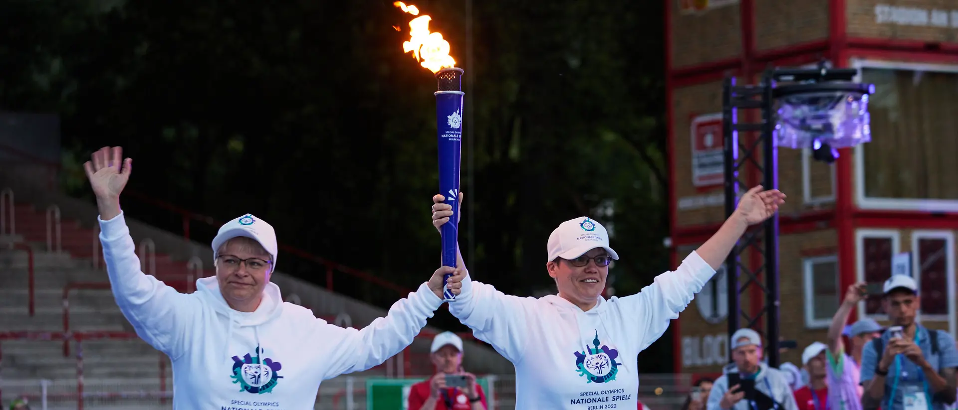 Zwei ehrenamtliche Helferinnen tragen eine brennende Fackel bei den Special Olympics.