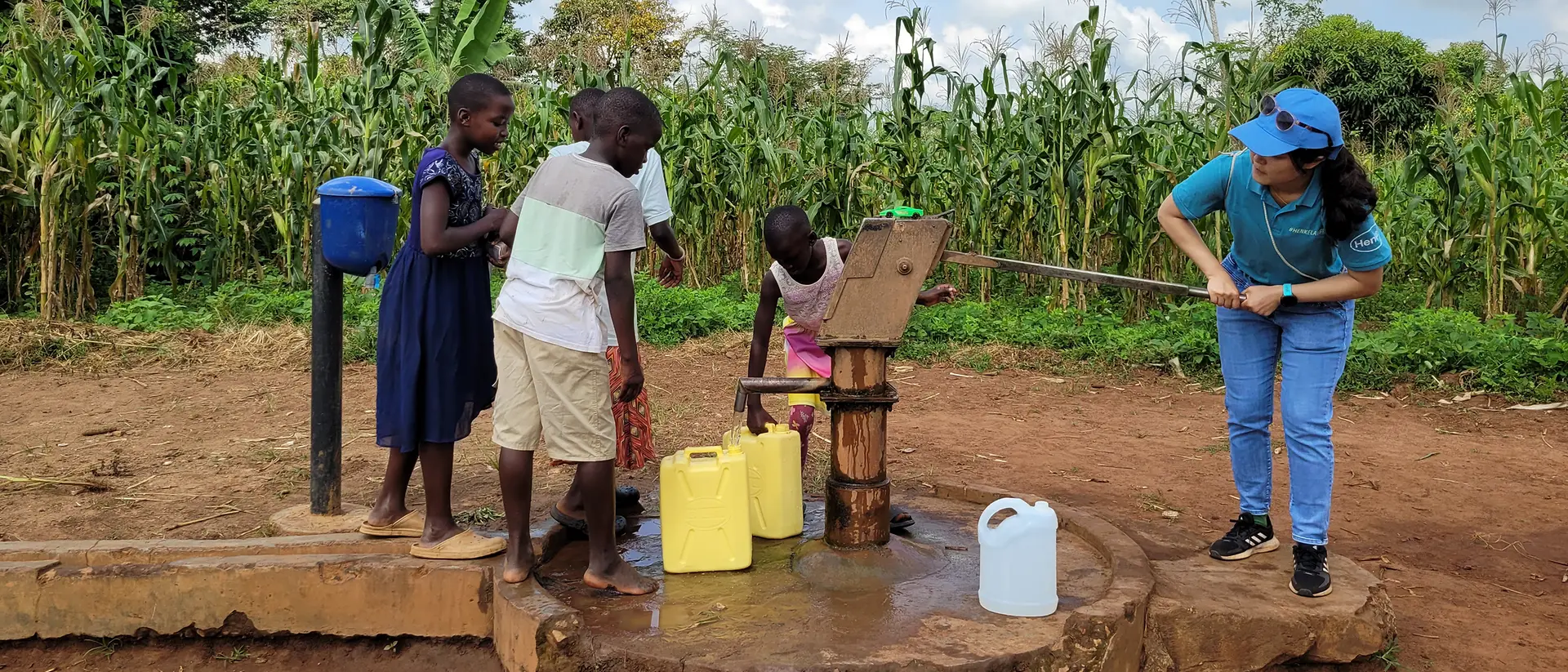 Eine ehrenamtliche Helferin holt zusammen mit Kindern Wasser von einem Brunnen.