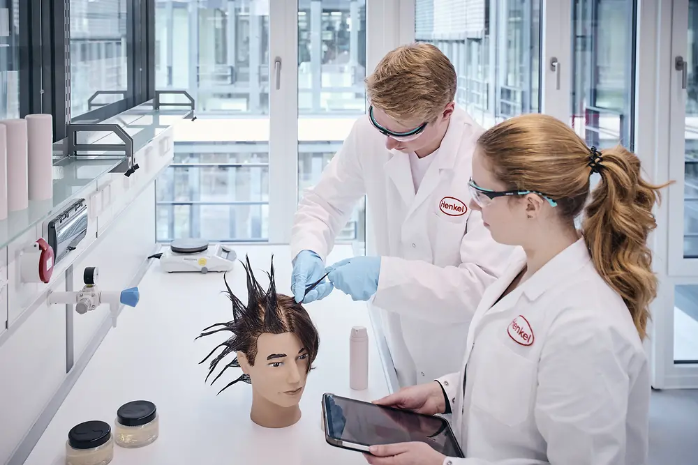 Zwei Labormitarbeiter:innen führen Tests an einer Puppe mit gestylten Haaren durch.