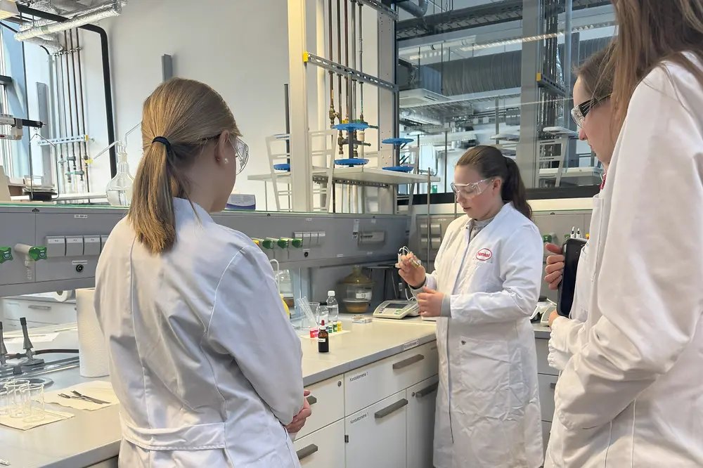 Ein Mädchen steht im Labor und experimentiert mit einem kleinen Reagenzglas. Drei weitere Mädchen stehen drumherum. 