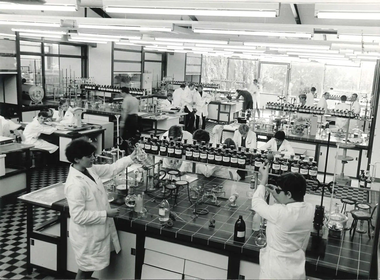 Chemielaborant:innen mit weißen Kitteln bei der Arbeit im Chemielaboratorium. 