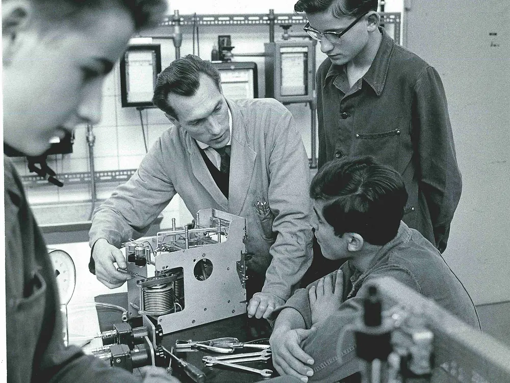 Ein Ausbilder zeigt drei Auszubildenden zum Elektroniker ein Gerät.