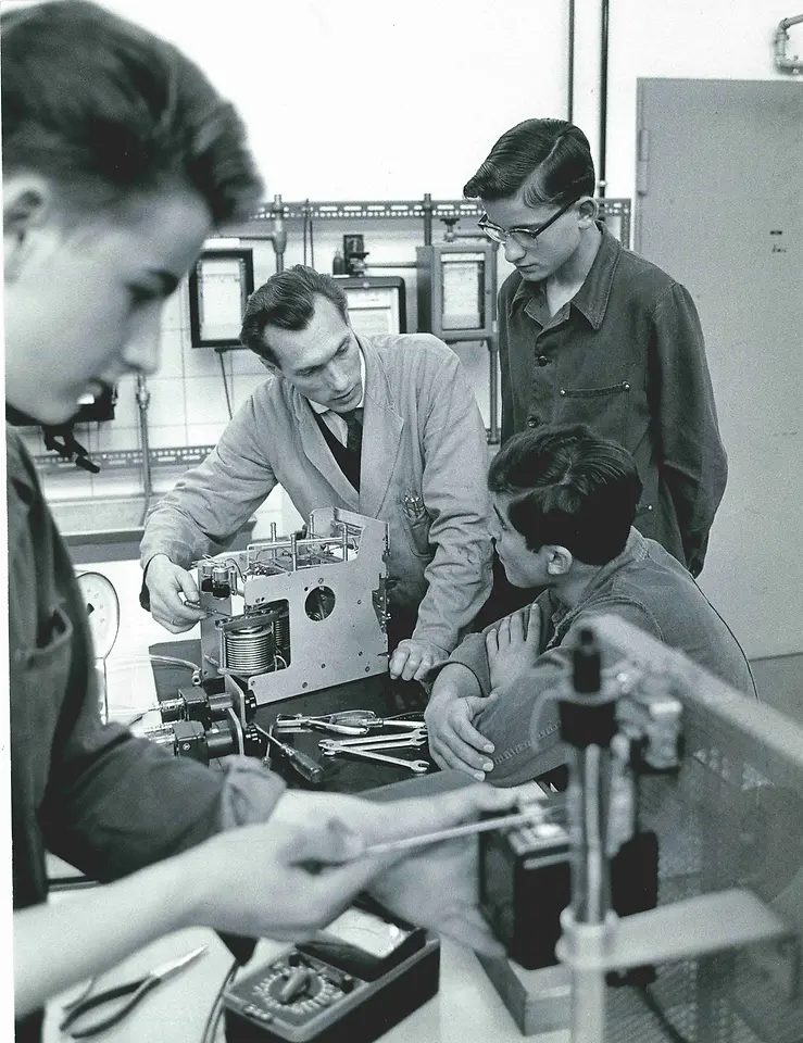 Ein Ausbilder zeigt drei Auszubildenden zum Elektroniker ein Gerät.