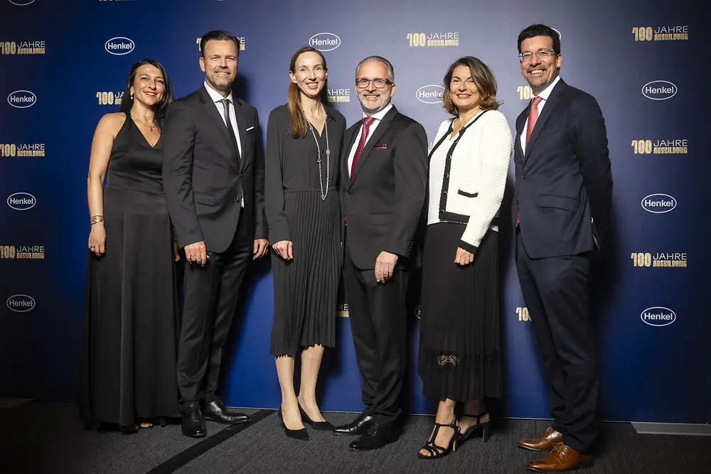 Funda Mutlu, Leiterin der Ausbildung bei Henkel, Oliver Wilhelms, Personalleiter von Henkel Deutschland und Schweiz, Dr. Simone Bagel-Trah, Vorsitzende des Aufsichtsrats und Gesellschafterausschusses, Carsten Knobel, CEO von Henkel, Sylvie Nicol, Mitglied des Vorstands, zuständig für Personal, Infrastruktur und Nachhaltigkeit und Mark Dorn, Mitglied des Vorstands, zuständig für den Unternehmensbereich Adhesive Technologies stehen vor einer Fotowand. 