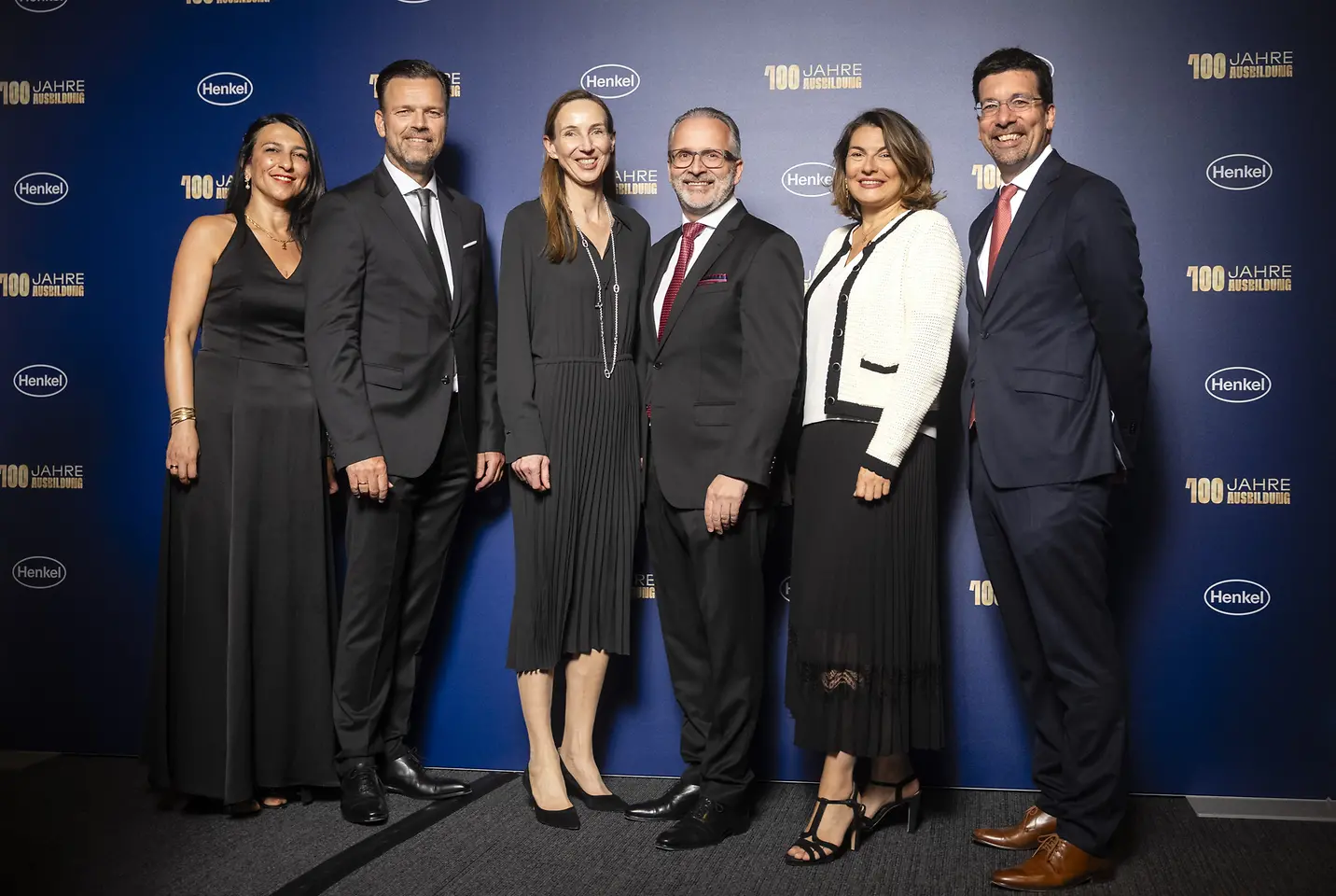 Funda Mutlu, Leiterin der Ausbildung bei Henkel, Oliver Wilhelms, Personalleiter von Henkel Deutschland und Schweiz, Dr. Simone Bagel-Trah, Vorsitzende des Aufsichtsrats und Gesellschafterausschusses, Carsten Knobel, CEO von Henkel, Sylvie Nicol, Mitglied des Vorstands, zuständig für Personal, Infrastruktur und Nachhaltigkeit und Mark Dorn, Mitglied des Vorstands, zuständig für den Unternehmensbereich Adhesive Technologies stehen vor einer Fotowand. 