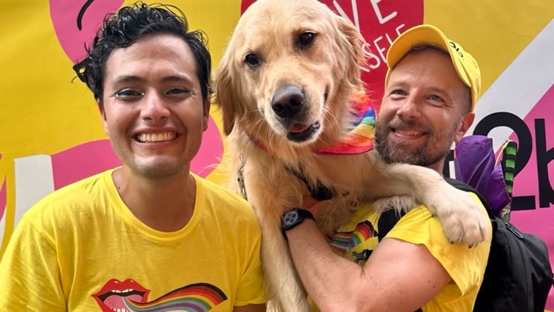 Ein Foto von Luis und James, die einen Hund in den Armen halten, got2b-T-Shirts tragen und bei einer Pride-Veranstaltung in die Kamera lächeln. 