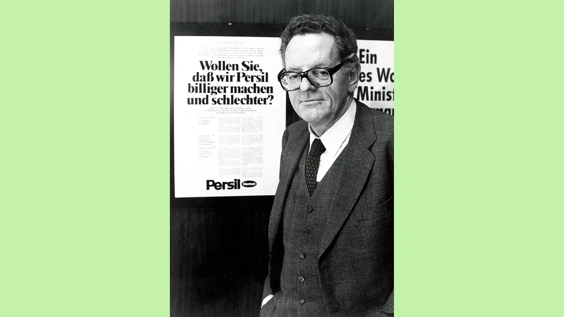 Schwarz-weiß Foto von Dr. Helmut Sihler in dunklen 3-Teiler und weißem Hem mit gemusteter Kravatte. Er steht seitlich, aber der Kamera zugewandt neben einem Plakat mit der Überschrift „Wollen Sie, daß wir Persil billiger machen und schlechter?“