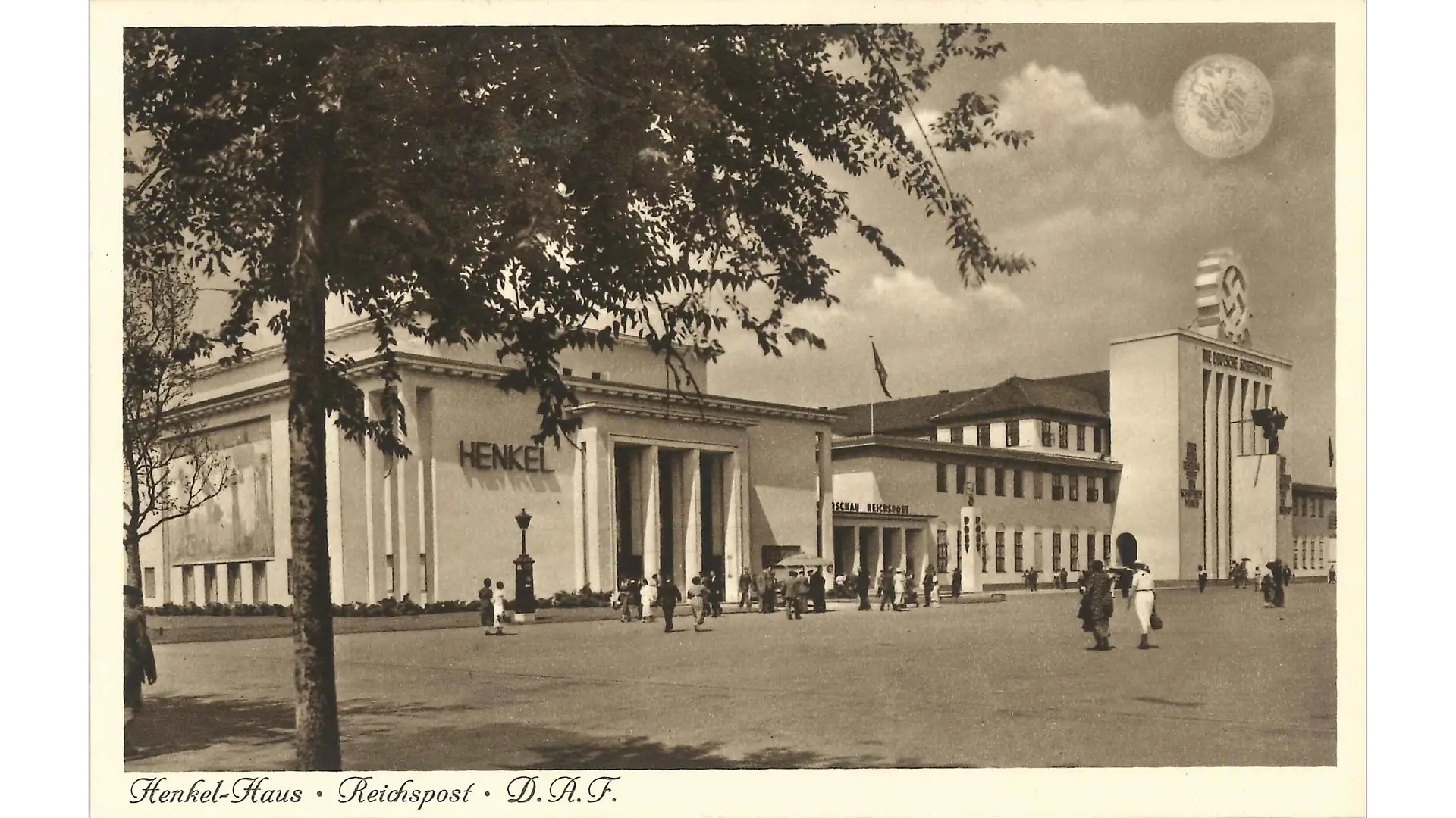 Der Henkel-Pavillon auf der Reichsaustellung „Schaffendes Volk“. Obwohl der Baustil eher schlicht gehalten ist, wirkt das Gebäude durch seine enorme Größe und die hohen Säulen, die in die Fassade integriert wurden, sehr prachtvoll – insbesondere, im Vergleich zum eher klein erscheinenden Gebäude daneben. Links neben dem Haupteingang ist groß der Firmenname Henkel angebracht.